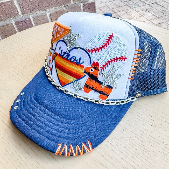 Navy trucker hat with white foam back, customized with fun Astros themed patches. Perfect for adding a touch of fun to any outfit. Includes a convenient 9" removable paperclip chain. Cap is hand embroidered by Jazmin, and rhinestone rivets are placed on right side of hat bill. Embroidery and rivets are permanent.