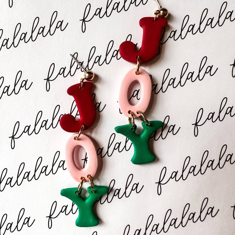 Make some holiday cheer with these JOY Christmas Dangle Earrings! Crafted from durable polymer clay and boasting a merry mix of pink, red, and green, they're sure to become your favorite seasonal accessory. Perfect for a bit of jolly jangling in your ears!