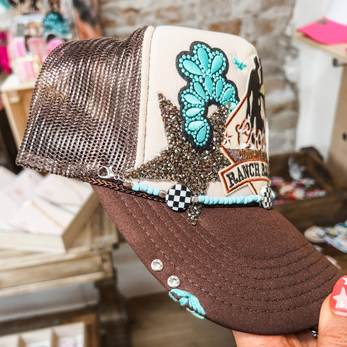 Brown trucker hat with tan foam back, customized with themed patches. Perfect for adding a touch of fun to any outfit. Includes a convenient 9" removable paperclip chain. Cap is hand embroidered by Jazmin, and rhinestone rivets are placed on right side of hat bill. Embroidery and rivets are permanent.