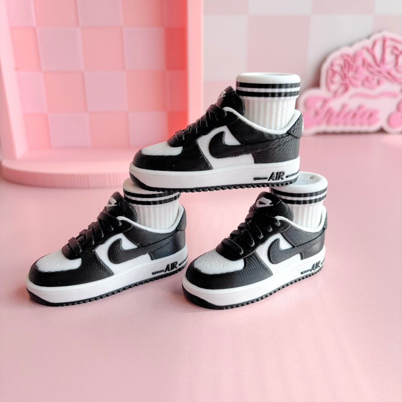 Three pairs of 3d printed sneakers in pink, blue, and black on a pink platform with a checkered wall background.