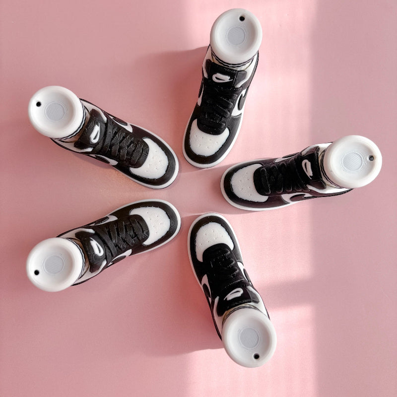 Three pairs of 3d printed sneakers in pink, blue, and black on a pink platform with a checkered wall background.