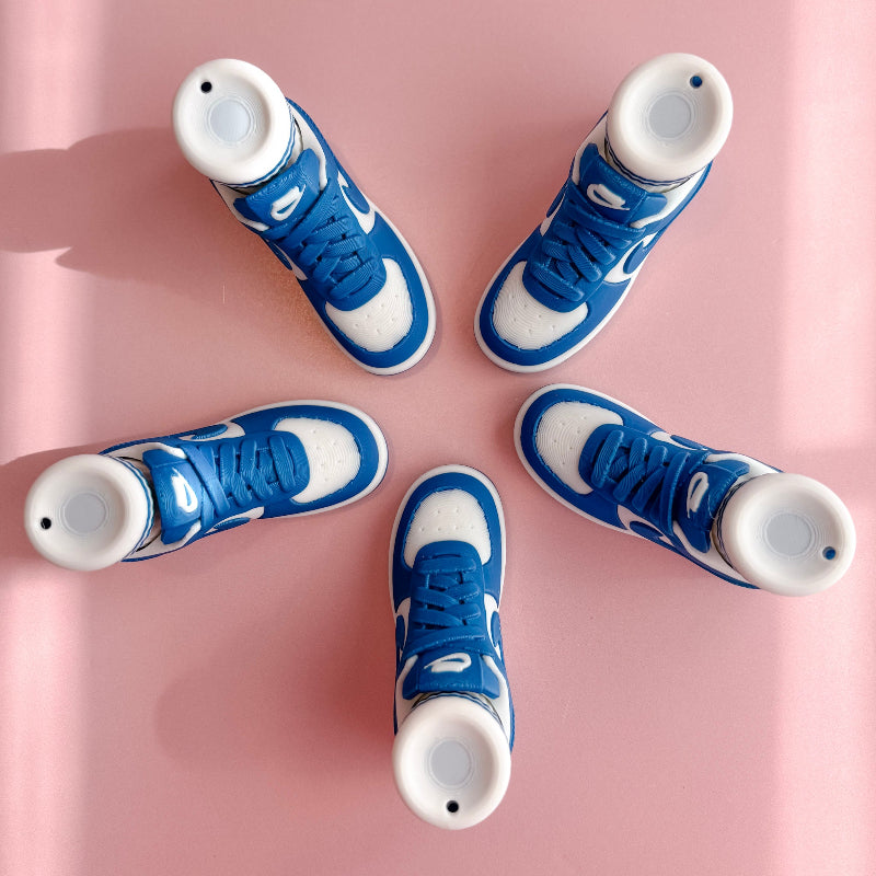 Three pairs of 3d printed sneakers in pink, blue, and black on a pink platform with a checkered wall background.