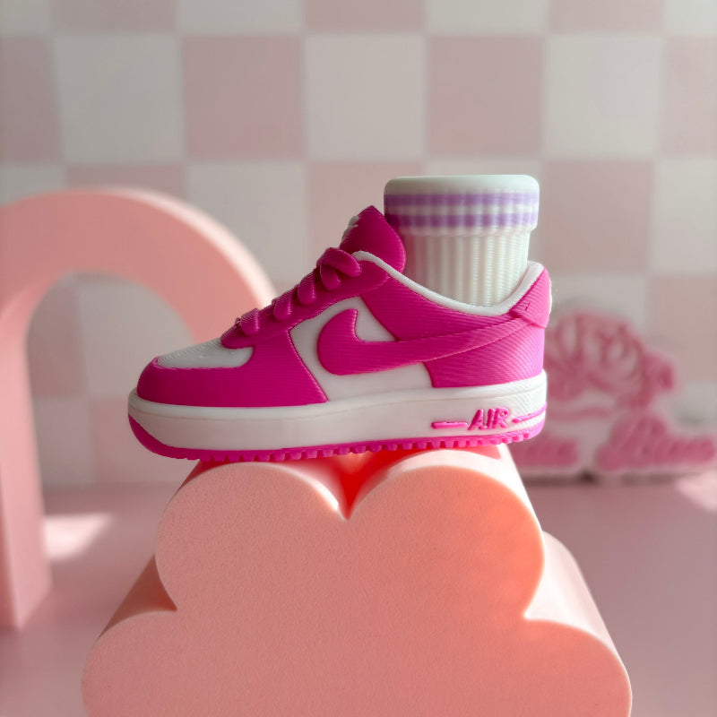 Three pairs of 3d printed sneakers in pink, blue, and black on a pink platform with a checkered wall background.