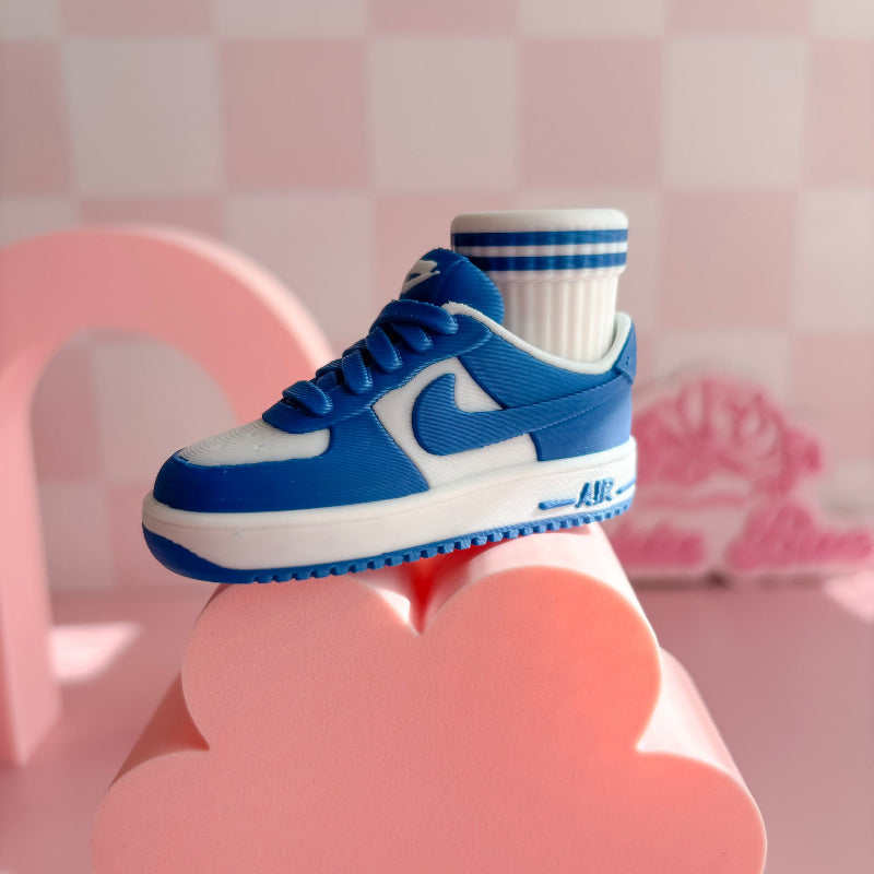 Three pairs of 3d printed sneakers in pink, blue, and black on a pink platform with a checkered wall background.