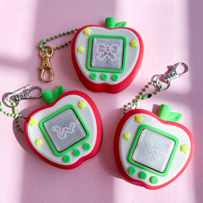 Three red and green fidget clicker resembling a Tamagotchi on a pink background.