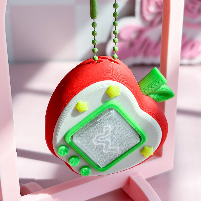 Red and green toy apple pixel fidget clicker with a screen on a pink stand