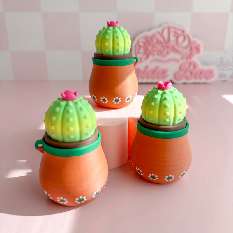 Three cactus-shaped decorative items on a pink surface with a blurred background.