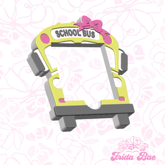 School bus-shaped phone holder with pink bow on a pink floral background, branded 'Frida Bae'.