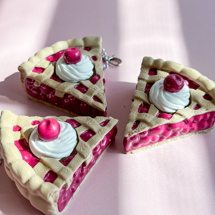 Three slices of cherry pie with whipped cream and a cherry on top on a pink background fidget clicker