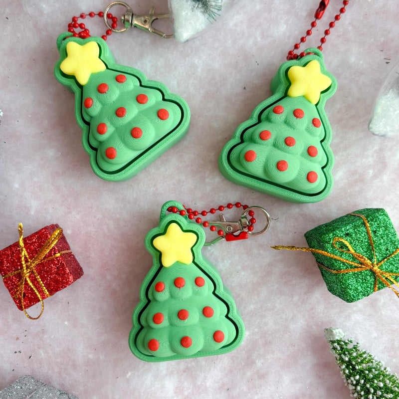 Green Christmas tree-shaped fidget clicker ornaments with red dots and yellow stars on a decorative background.