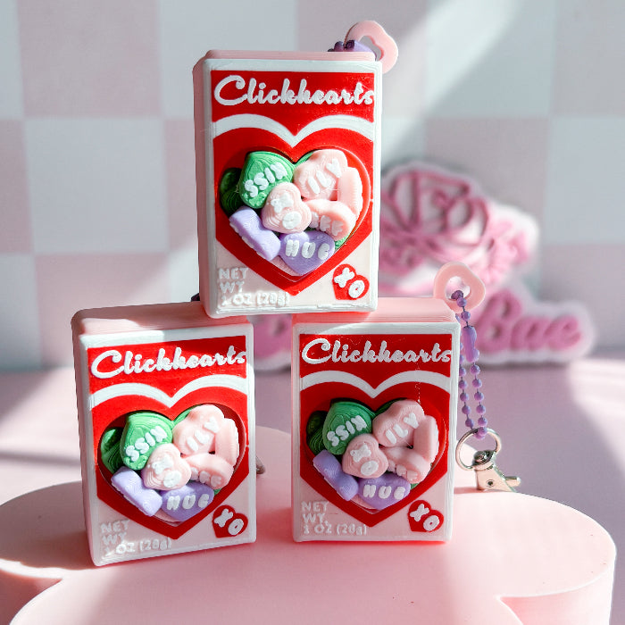 Three 'Clickhearts' candy boxes with a heart design on a pink surface.