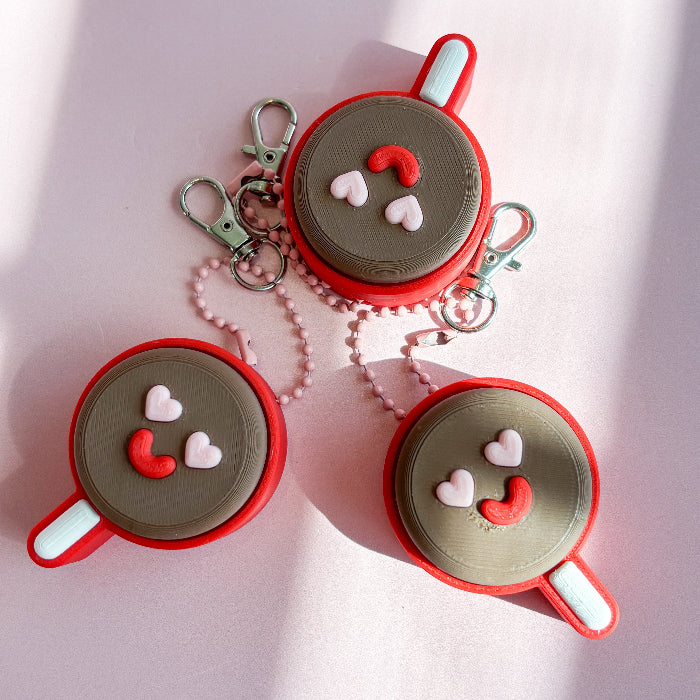 Three red and gray keychains with smiley face designs on a pink background