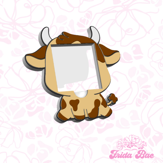 Cow-shaped photo frame on a pink floral background with 'frida Bae' branding.