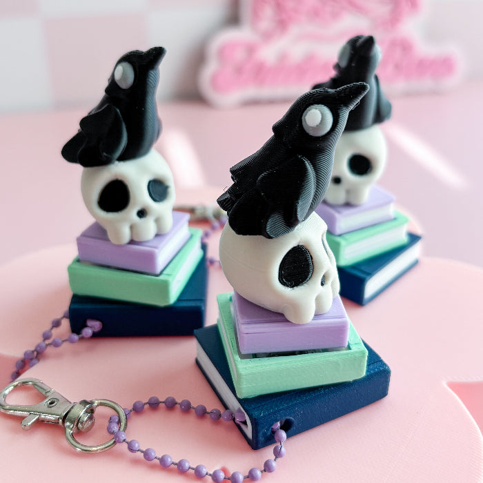 Skull-shaped keychains on colorful books with a pink background