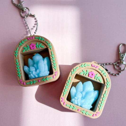 Two decorative keychains with blue crystal-like designs on a pink background