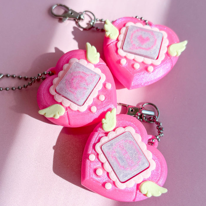 Three pink heart-shaped keychains with a central square design on a pink background