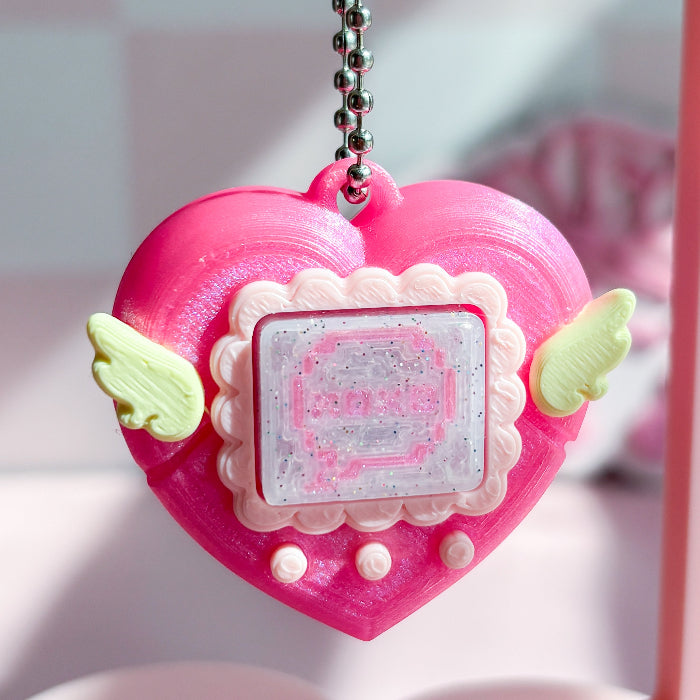Pink heart-shaped keychain with angel wings on a blurred background