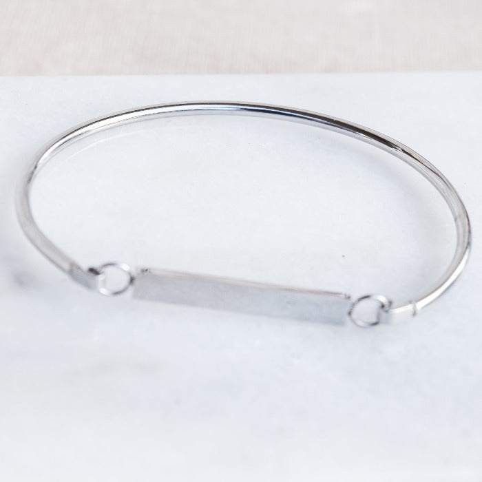 Elevate your everyday look with our FLAT BAR BRACELET in SILVER This minimalist, chic design features a bangle band and a blank bar centerpiece, perfect for personalization with a special message or date. Versatile and stylish, it's the perfect piece for any outfit, from casual to weekend attire.