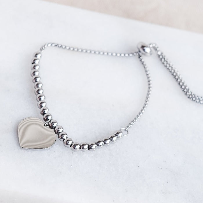 Experience the perfect blend of style and sentiment with our RAYNE CORAZON BEADED BRACELET in SILVER! Crafted from durable stainless steel, this adjustable bracelet features an engravable heart pendant charm, making it the ideal personalized accessory for any special occasion. The adjustable chain ensures a comfortable fit for all wrist sizes. 
