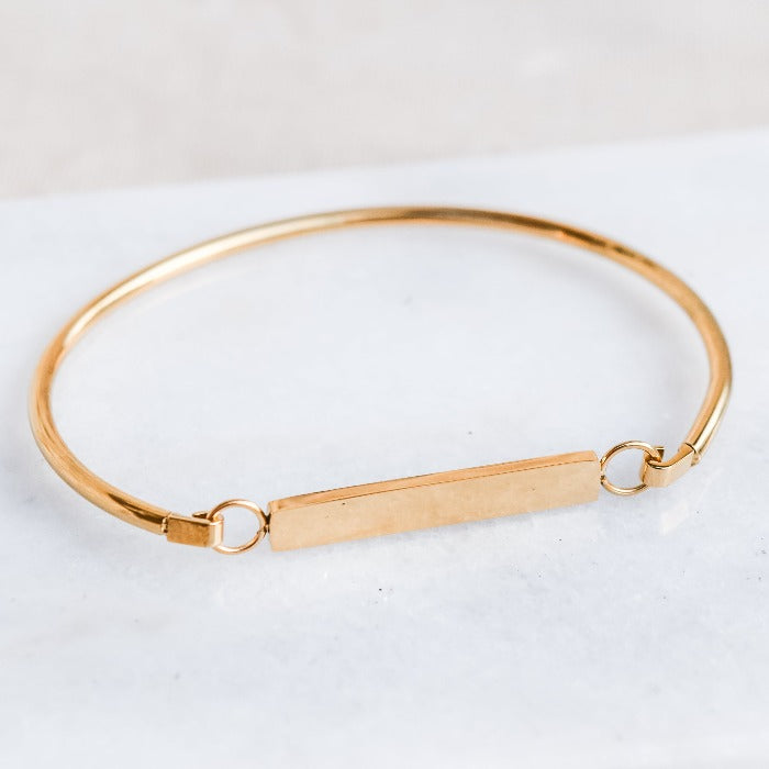 Elevate your everyday look with our FLAT BAR BRACELET in GOLD. This minimalist, chic design features a bangle band and a blank bar centerpiece, perfect for personalization with a special message or date. Versatile and stylish, it's the perfect piece for any outfit, from casual to weekend attire.