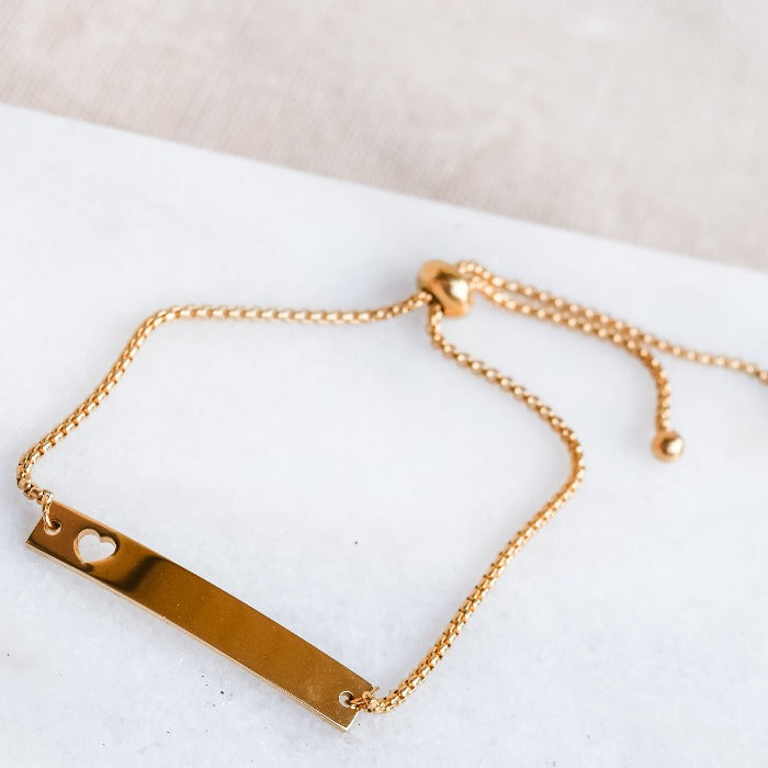 This polished gold heart bar bracelet is the perfect symbol of love. Its adjustable chain fits a wide range of wrist sizes, making it a versatile and timeless piece. The heart-shaped cutout adds an extra touch of warmth and affection, making it a cherished piece in anyone's jewelry collection.