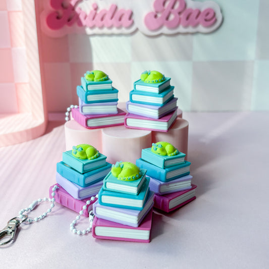 stack of colorful books with green dragon on top on pink background