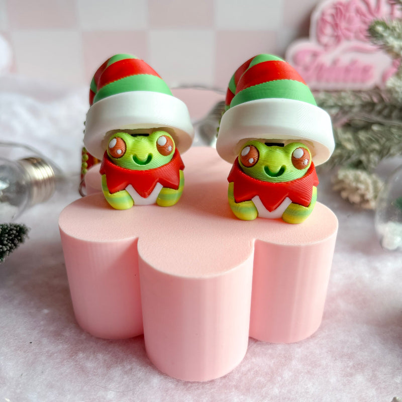 Two green characters in festive outfits on pink stands with a blurred decorative background