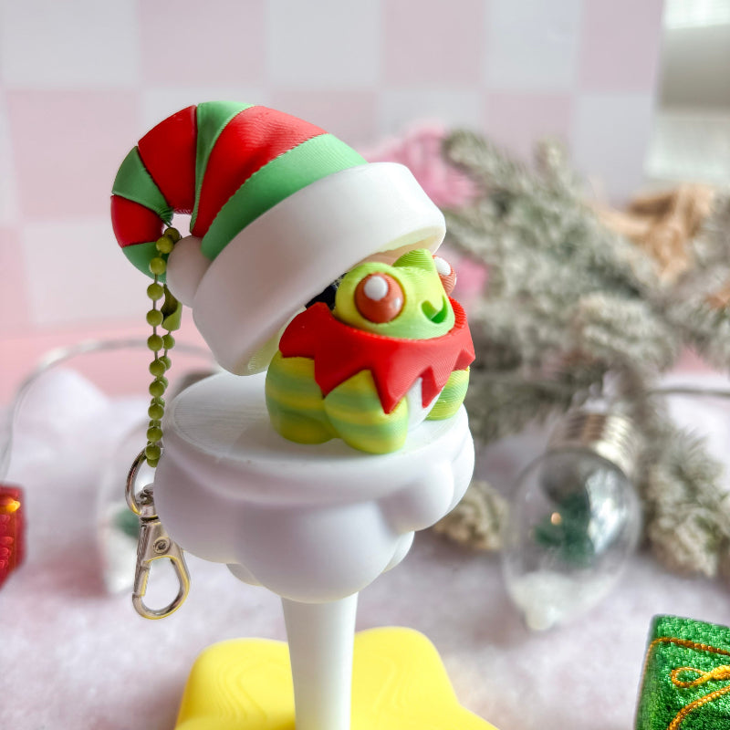 Decorative Christmas-themed keychain with a small figure on a stand against a blurred background.