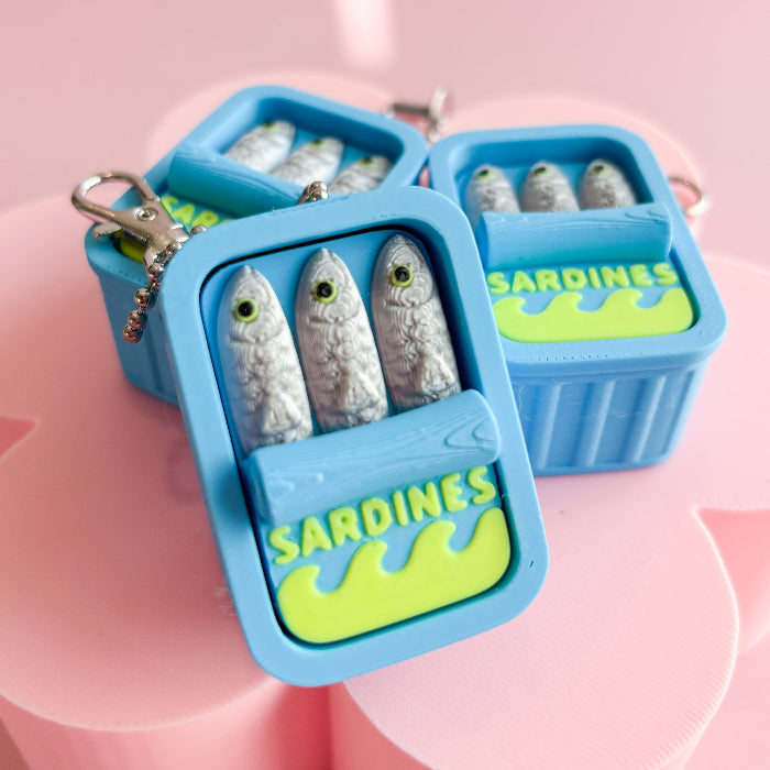 Blue sardine-shaped fidget clickers with sardine figurines on a pink background