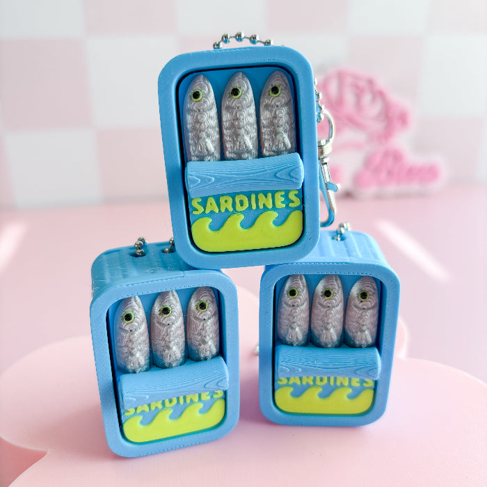 Blue sardine-shaped fidget clickers with sardine figurines on a pink background