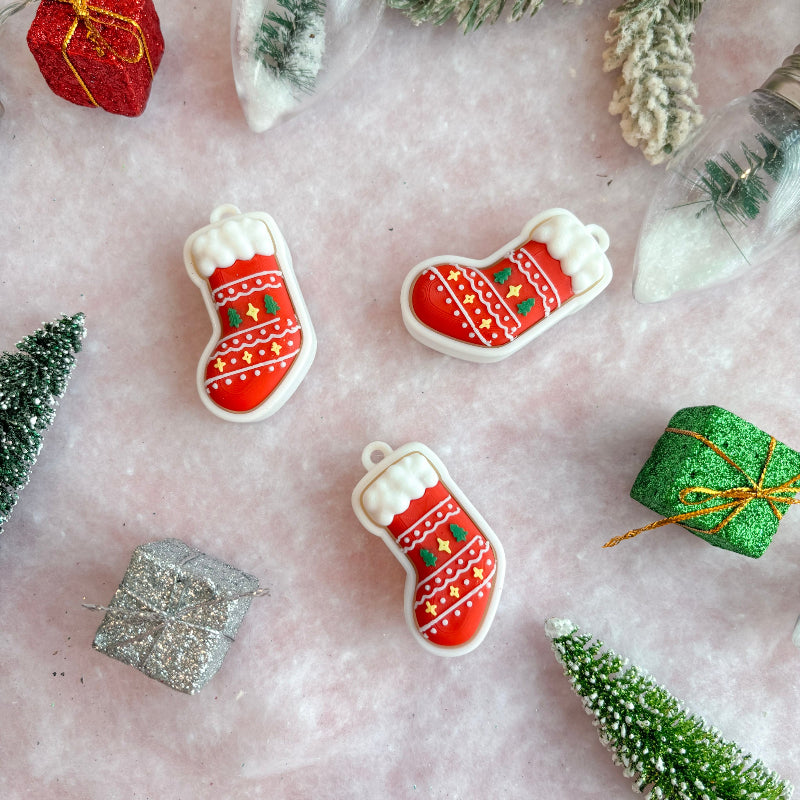 Christmas-themed fidget clickers shaped like stockings and gift boxes on a decorative surface with trees and presents.