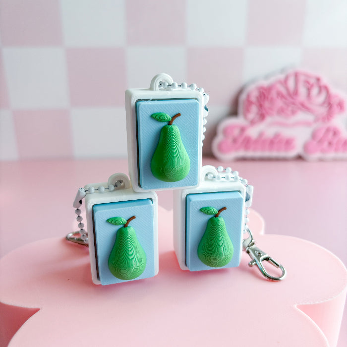 Mexican loteria fidget clicker with  pear-shaped charms on light blue square backgrounds with a pink checkered background.