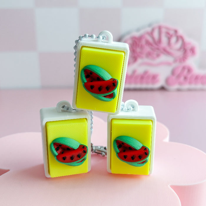 Mexican loteria fidget clicker with watermelon-themed rubber stamps on a pink surface with a blurred background.