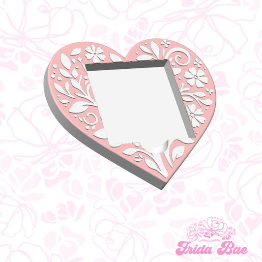 Heart-shaped stencil with floral design on a pink patterned background, featuring the brand 'frida Bae'.