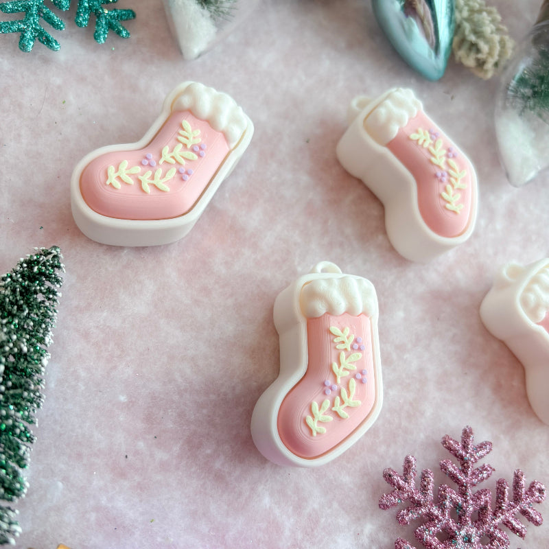 Pink stocking-shaped clickers with white icing on a pink surface with decorative elements.