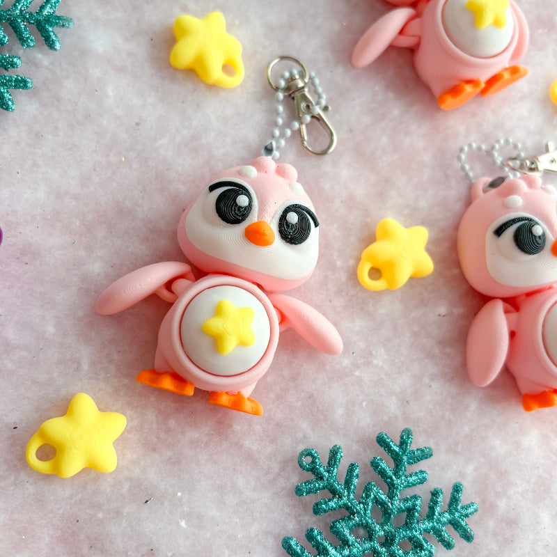 Colorful penguin keychains with snowflake and star decorations on a textured surface.
