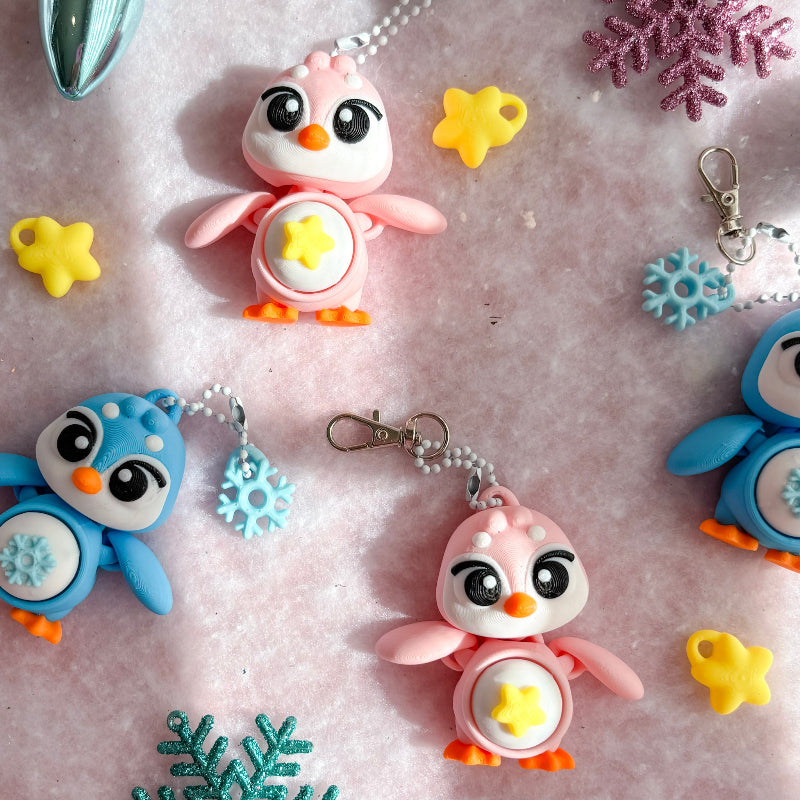 Colorful penguin keychains with snowflake and star decorations on a textured surface.