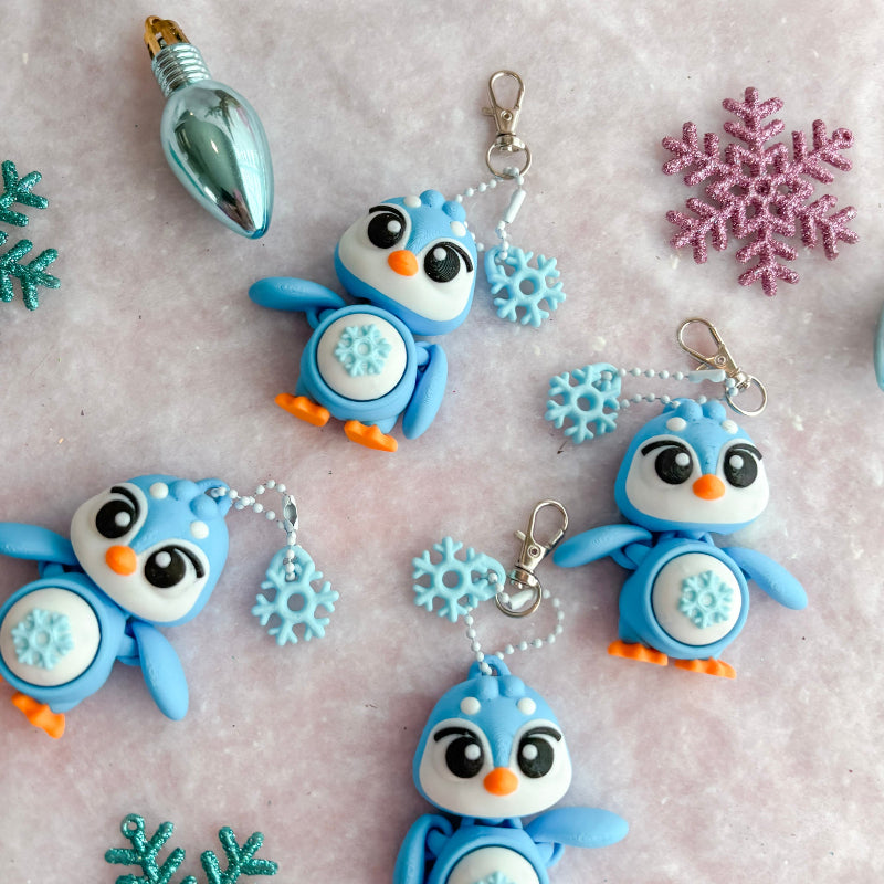 Colorful penguin keychains with snowflake and star decorations on a textured surface.