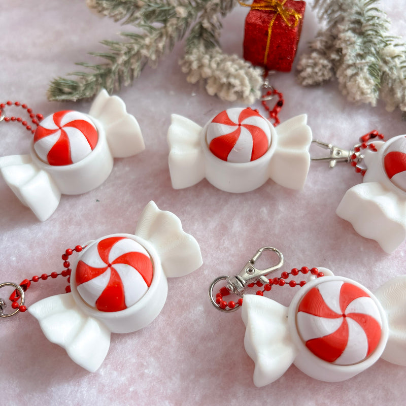 White candy-shaped keychains with red and white peppermint candies on a light pink surface with decorative elements.