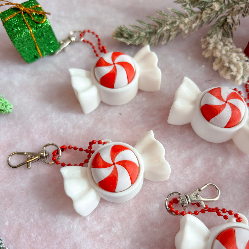 White candy-shaped keychains with red and white striped centers on a light pink surface with decorative elements.