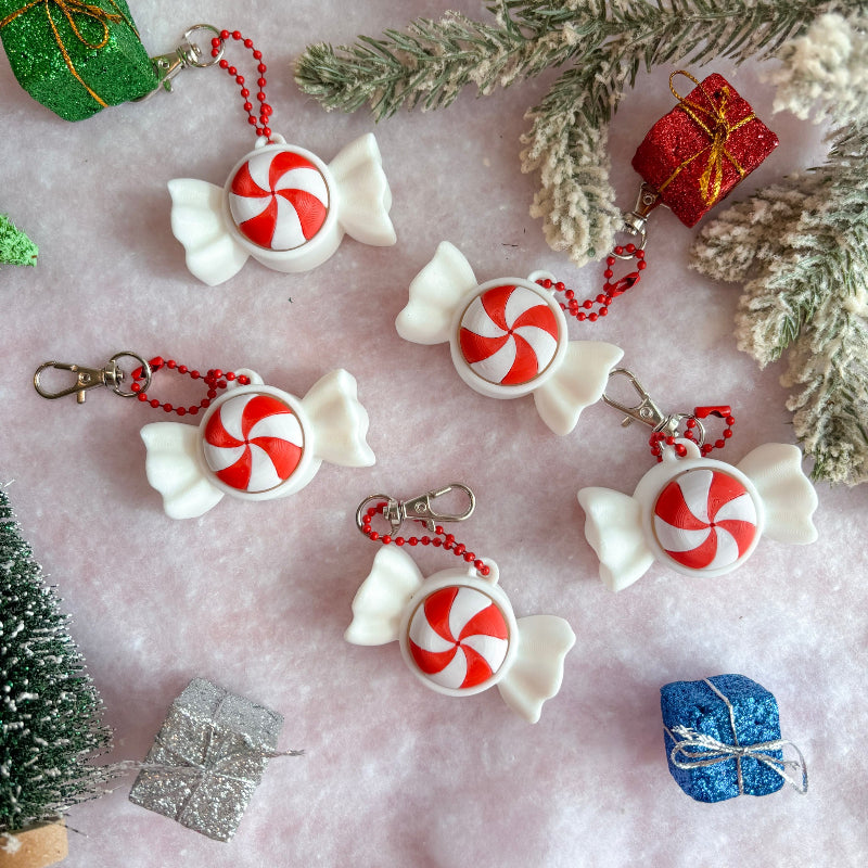 Decorative keychains shaped like candies and wrapped gifts on a festive background with Christmas decorations.