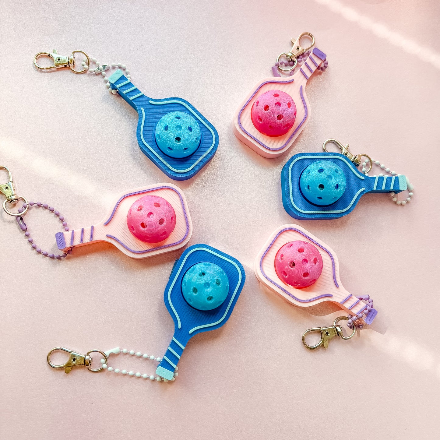Colorful keychains shaped like pickleball paddles on a light pink background