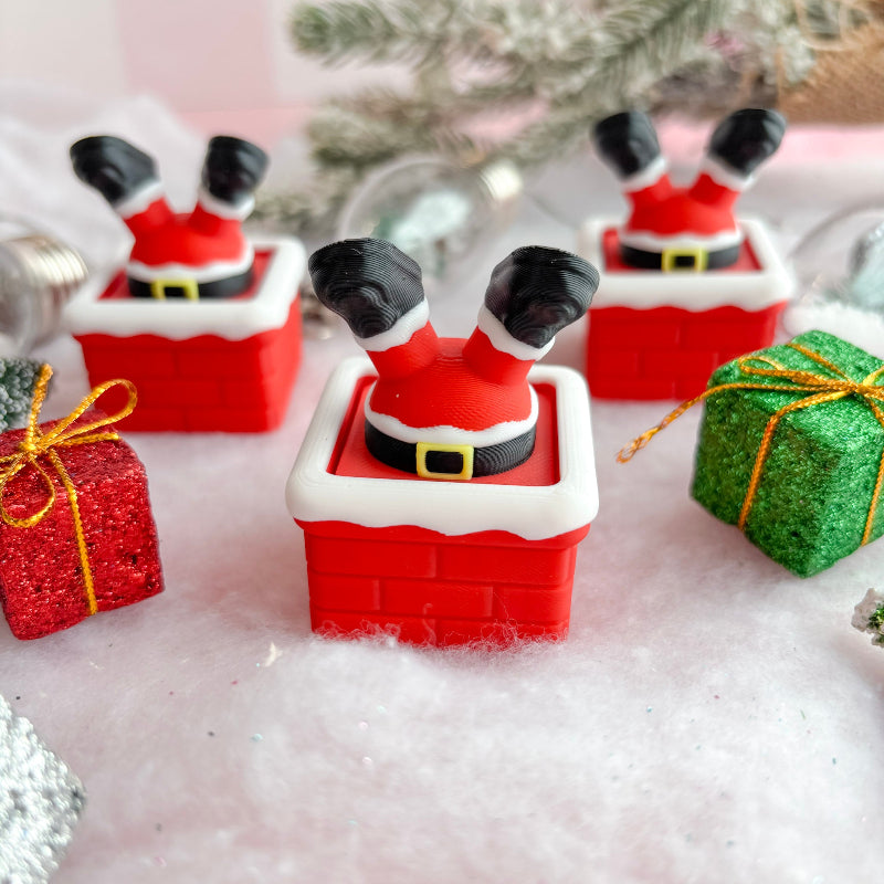 Christmas-themed figurines of  Santa stuck in chimney with presents and a tree in the background.