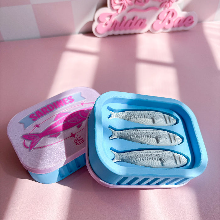 Sardine fidget clicker fish-shaped mold on a pink surface with 'Sardines' branding.