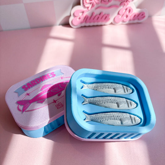 Sardine fidget clicker fish-shaped mold on a pink surface with 'Sardines' branding.