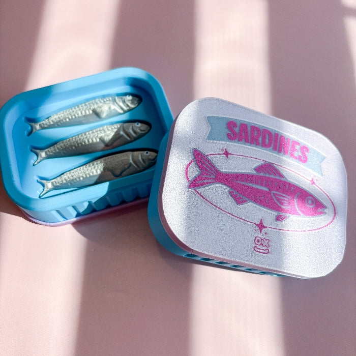 Sardine fidget clicker fish-shaped mold on a pink surface with 'Sardines' branding.
