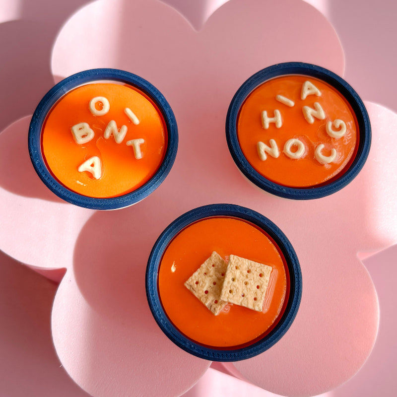 Three small orange containers with blue rims on a pink flower-shaped plate.