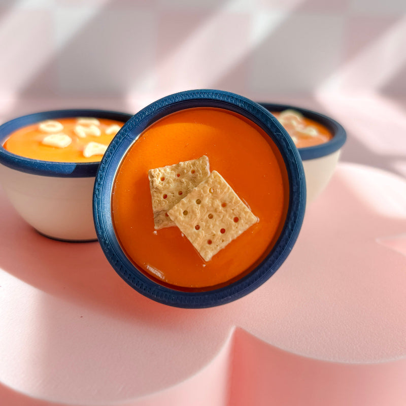 Three small bowls of soup with crackers on a pink surface