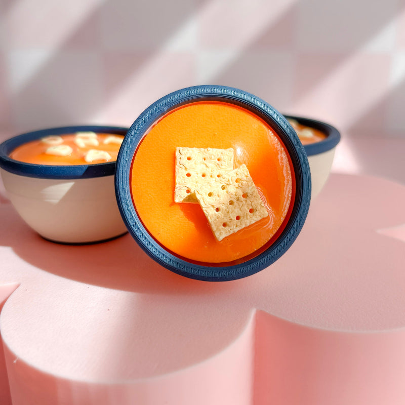 Bowl of soup with a cracker on a pink background