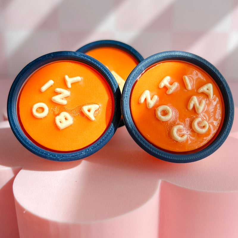 Three round orange objects with lettered decorations on a pink background